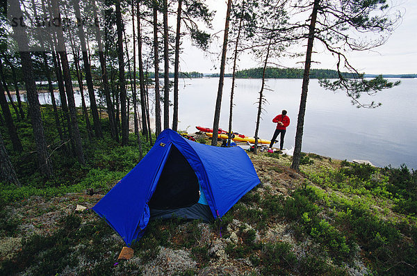 Eine blaue Zelt von einem ruhigen See in Schweden einer Person und zwei Kajaks im Hintergrund.