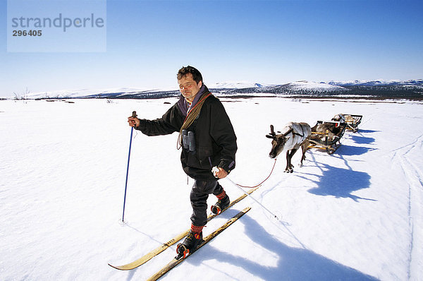 Ein Mann auf Skiern mit einem Hirsch und Schlitten hinter.