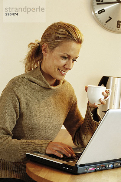 Eine Frau mit einer Kaffeetasse auf einem Laptop arbeiten.