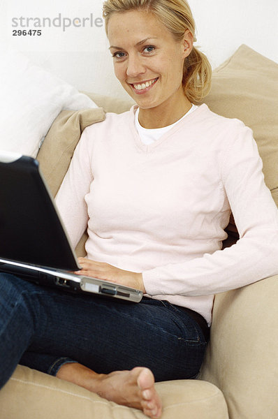 Eine Lächelnde Frau mit einem Laptop in einem Sofa.