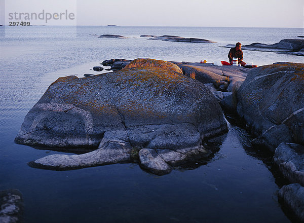 Ein Mann sitzt auf flat Rock am Meer.