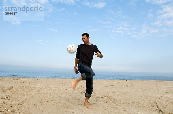 Caucasian männlichen Fußball am Strand zu üben