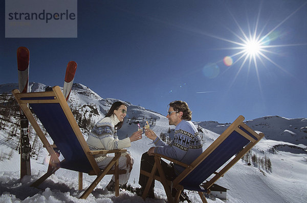 Paar auf Liegestühlen im Schnee sitzend  Gläser haltend  Seitenansicht