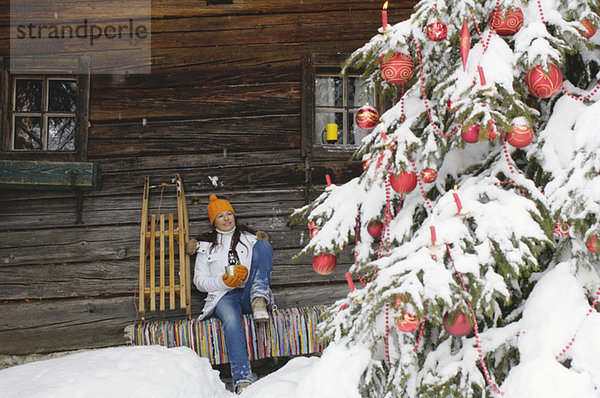 Frau sitzt vor der Berghütte und schaut auf den Weihnachtsbaum