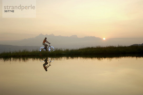 Österreich  Alpen  Frau mit dem Fahrrad am See  Seitenansicht