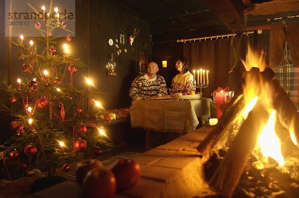 Paar am Tisch in der Almhütte mit Blick auf den Weihnachtsbaum