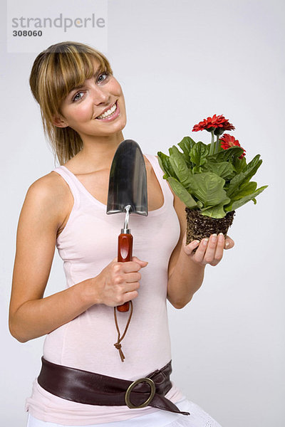 Junge Frau hält Topfpflanze und Kelle  lächelnd