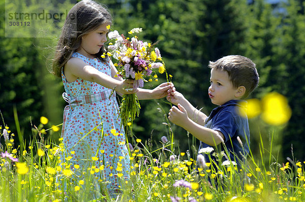 Mädchen und kleiner Junge mit Blumenstrauß auf der Sommerwiese