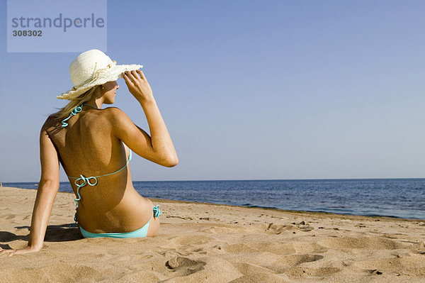 Junge Frau am Strand sitzend  Rückansicht