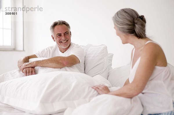 Erwachsenes Paar auf dem Bett sitzend  Mann lächelnd