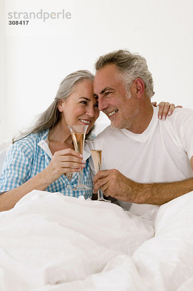 Ein reifes Paar auf dem Bett  das Champagner trinkt  lächelnd