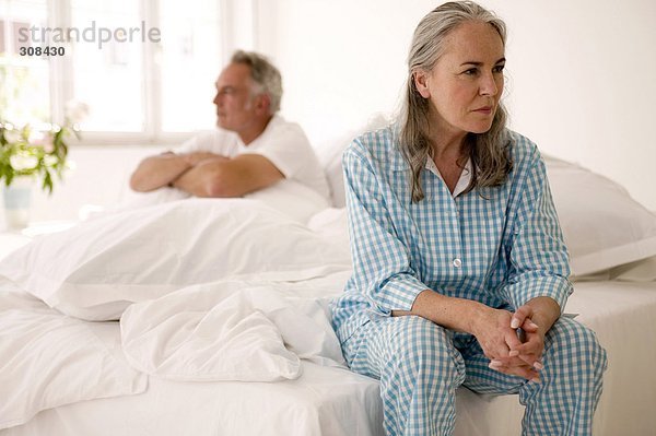 Erwachsenes Paar auf dem Bett sitzend (Fokus auf die Frau im Vordergrund)