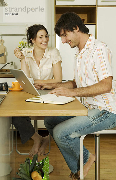 Junges Paar in der Küche  Mann mit Laptop  lächelnd
