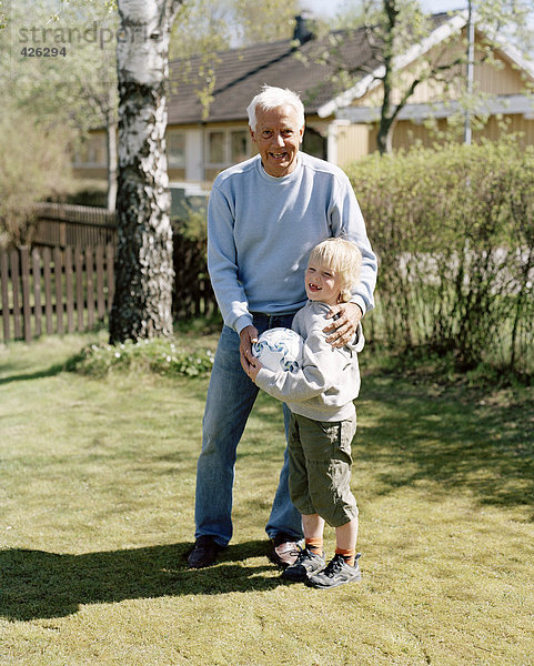 Großvater und Enkel mit einem Fußball in einem Garten.