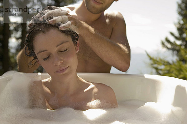 Young woman lying in bathtub  young man washing hair