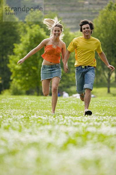 Junges Paar läuft auf der Wiese mit Hand in Hand