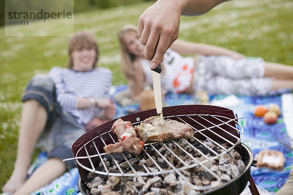 Fleisch auf dem Grill Teenager im Hintergrund