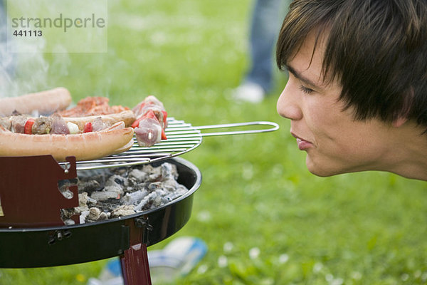 Junger Mann am Grill mit Fleisch  Seitenansicht  Nahaufnahme