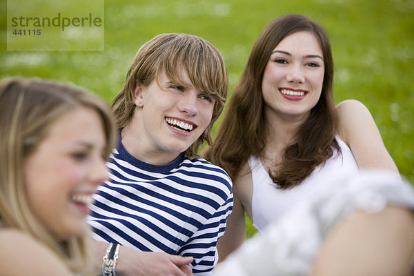 Junge Leute sitzen auf der Wiese und lächeln