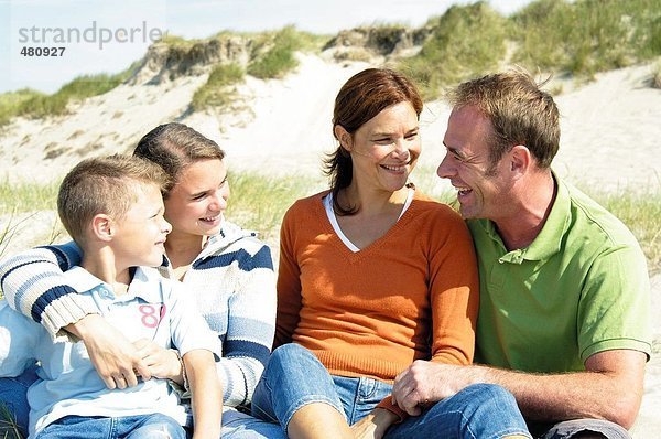 Familie sitzen am Strand und lächelnd