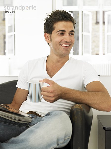 Ein Mann mit einer Tasse und eine Zeitung in einem Sessel.