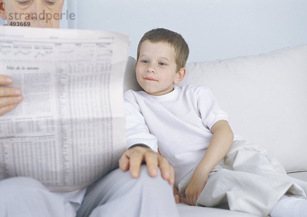 Junge sitzt auf dem Sofa neben Großvater  während er Zeitung liest.