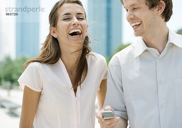 Junges Paar lacht  während der Mann das Handy hält.