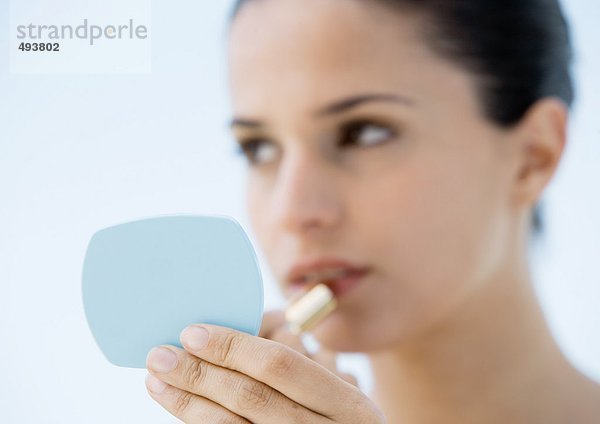 Frau setzt Lippenstift auf  Fokus auf Hand hält Spiegel im Vordergrund  Mund