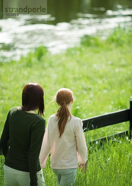 Frau und Mädchen gehen am Holzzaun entlang  Teich im Hintergrund