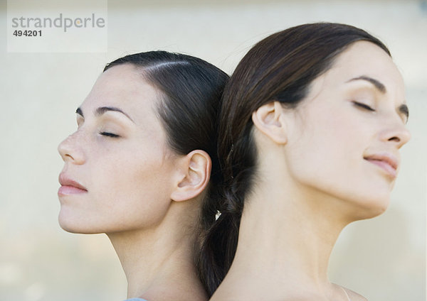 Zwei junge Frauen Rücken an Rücken mit geschlossenen Augen  Seitenansicht
