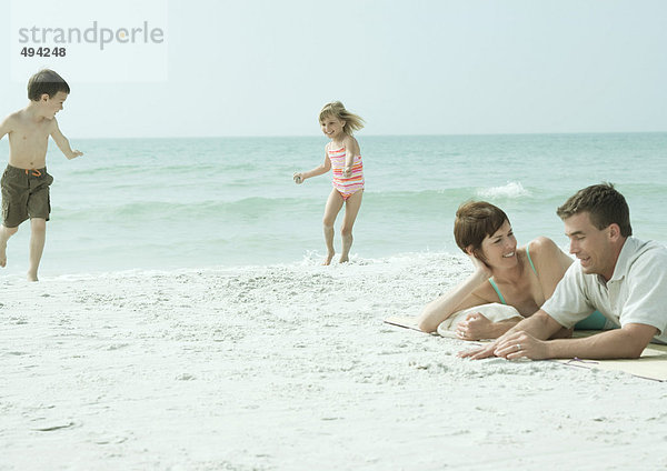 Familie am Strand  Eltern liegen auf Sand  während Kinder spielen