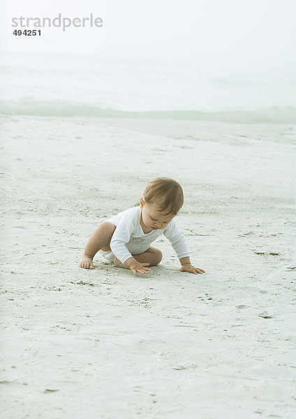 Baby sitzt am Strand  berührt Sand