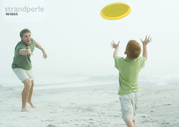 Vater und Sohn werfen Frisbee an den Strand