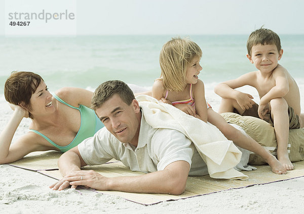 Familie am Strand  Eltern liegen auf der Matte  Kinder sitzen auf dem Rücken des Vaters.