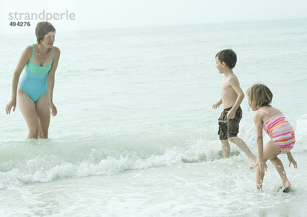 Familie am Strand  Mutter steht in den Wellen und schaut Kinder an  die ins Wasser kommen.
