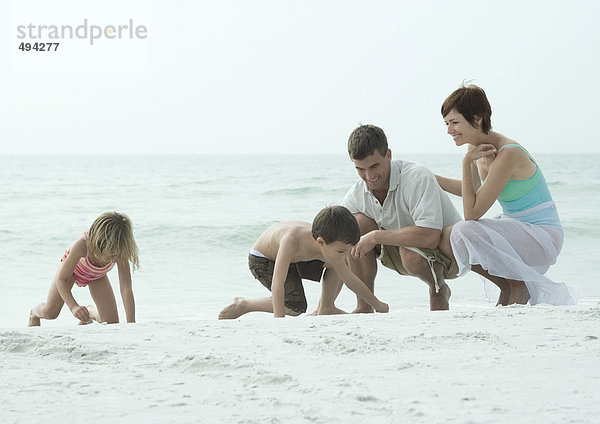 Familie am Strand  Kinder spielen auf Sand  während die Eltern zuschauen.
