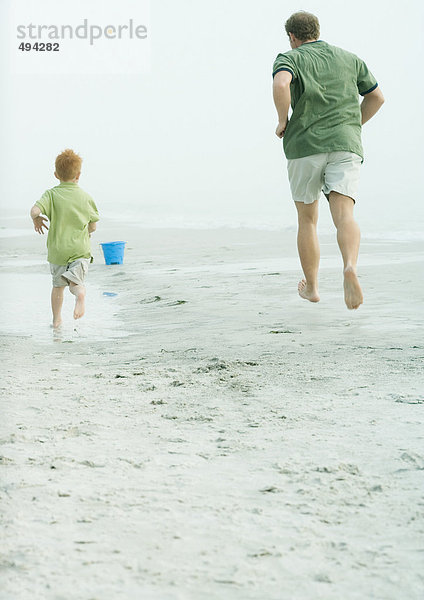 Vater und Sohn laufen am Strand  Rückansicht