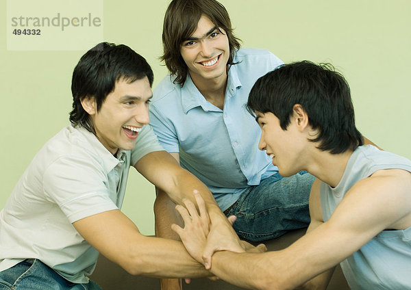Drei junge Männer  die sich die Hände umklammern.