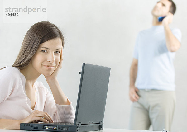 Frau mit Laptop und Mann mit Handy im Hintergrund