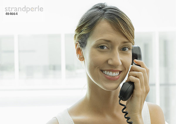 Frau mit Festnetztelefon  lächelnd vor der Kamera
