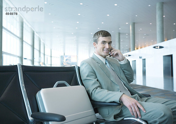 Geschäftsmann  der in der Flughafenlounge sitzt und sein Handy benutzt.
