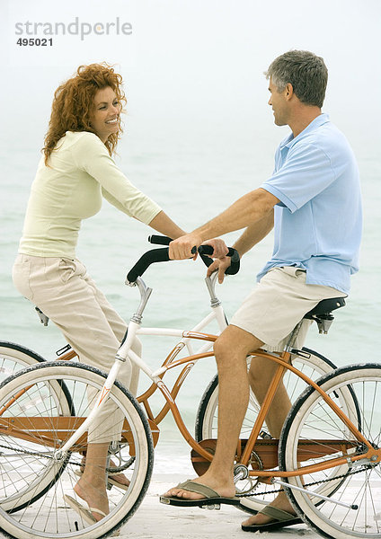 Paar von Angesicht zu Angesicht auf Fahrrädern  am Strand