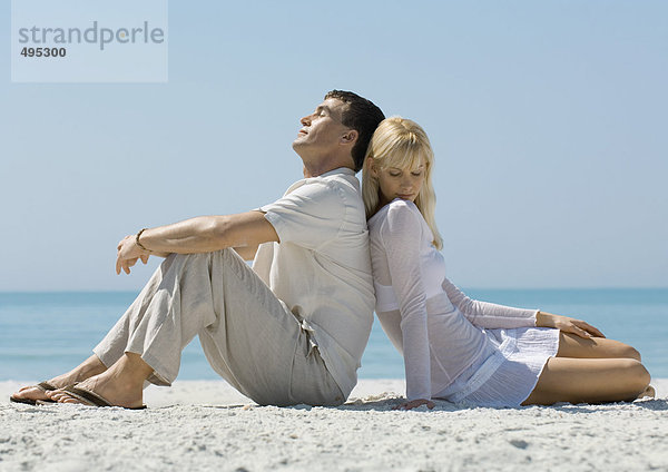 Paar am Strand sitzend  Rücken an Rücken