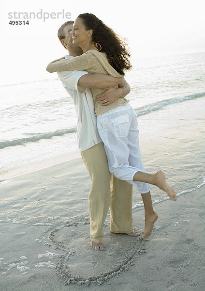 Paar in Herzform auf dem Strand stehend