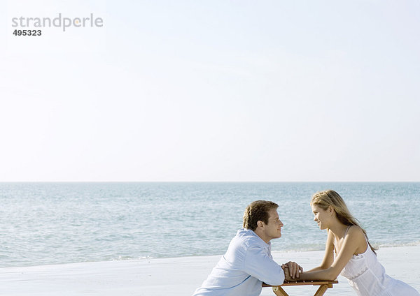 Ein Paar sitzt am Strand und schaut sich an.