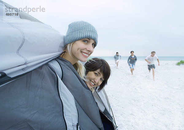 Am Strand ragen zwei junge Frauen aus dem Zelt  während Freunde in der Ferne zu ihnen rennen.