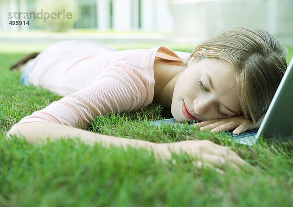 Teenagermädchen schläft mit Kopf auf Laptop  im Gras liegend