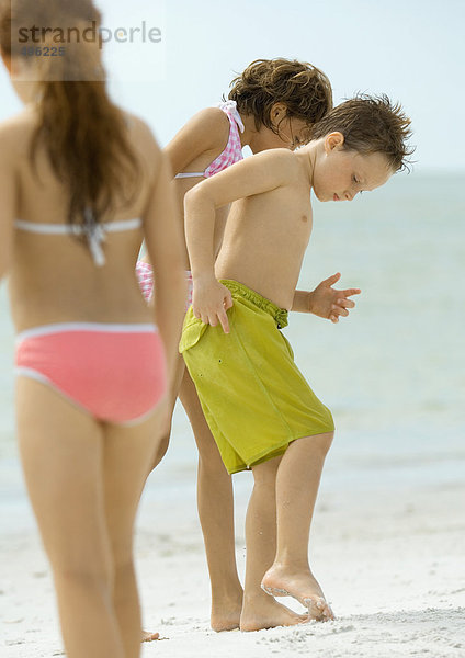 Kinder  die am Strand stehen und auf den Sand schauen.