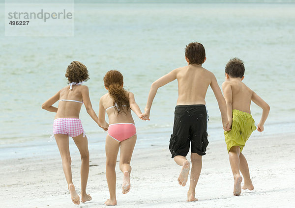 Vier Kinder halten sich an den Händen und rennen zum Wasser  am Strand  Rückansicht