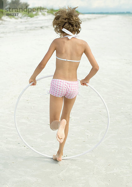 Mädchen läuft mit Kunststoffreifen am Strand